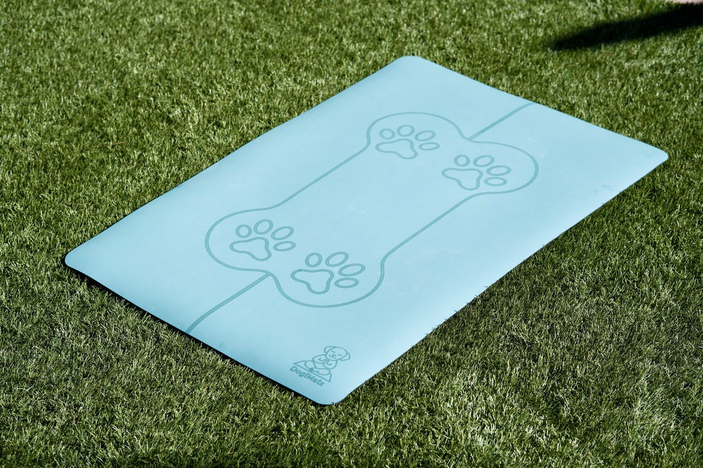 Turquoise DogiMat with bone and paw design on grass